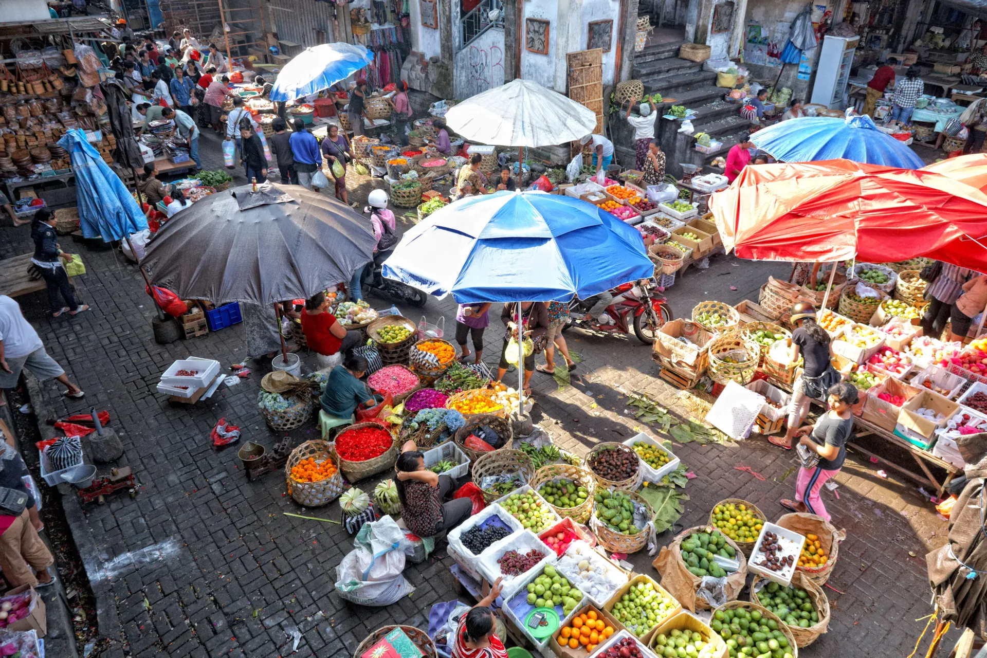 Mercado tradicional de Ubud, Bali, con puestos de frutas, flores y cestas bajo sombrillas de colores