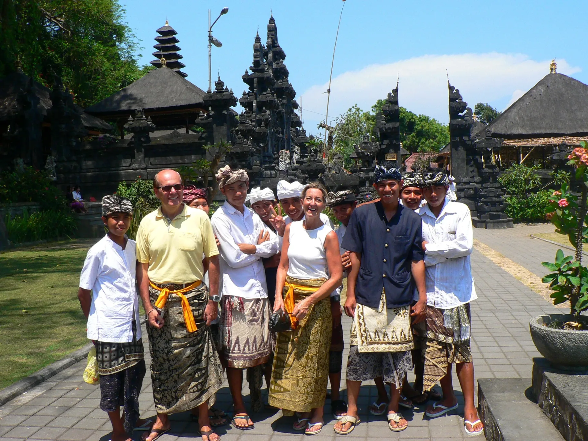 Una pareja con sarong posa junto a un grupo de jóvenes balineses en el templo local de Jimbaran, Bali, Indonesia